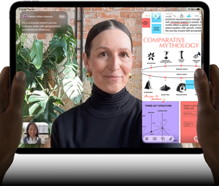 Widoczny od przodu ustawiony poziomo iPad Pro w kolorze gwiezdnej czerni, zaokrąglone rogi, czarna ramka wyświetlacza. Ręce trzymają urządzenie z lewej i prawej strony, na ekranie tłumaczona na żywo rozmowa przez FaceTime. Widać też aplikację edukacyjną z prezentacją „Comparative Mythology”, z tekstem, diagramami i odręcznymi notatkami