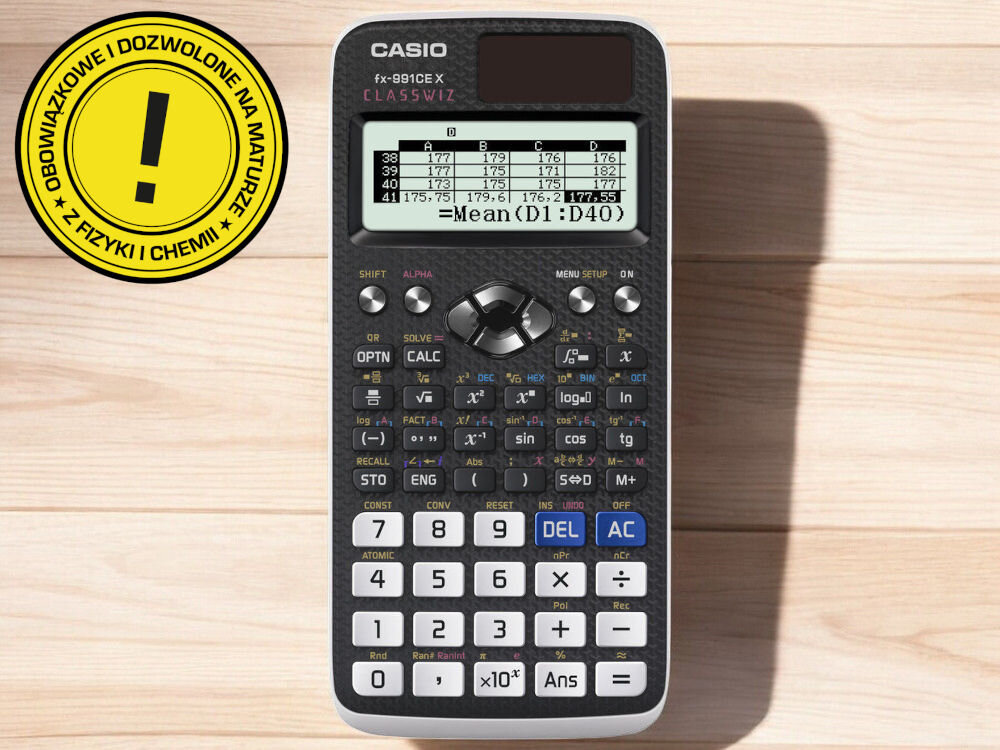 Na drewnianym tle znajduje się kalkulator CASIO FX-991CEX z wyświetlaczem pokazującym tabelę danych i obliczenie średniej. Obok kalkulatora widoczna jest żółta naklejka z tekstem: \'OBOWIĄZKOWE I DOZWOLONE NA MATURZE + Z FIZYKI I CHEMII +\'.