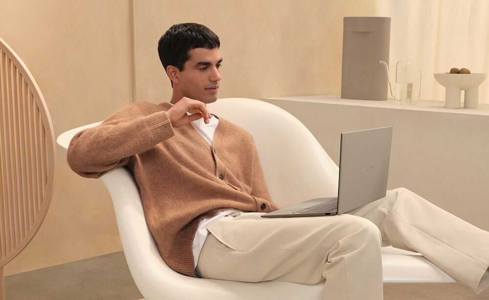 Mężczyzna w beżowym swetrze zrelaksowany w fotelu pracuje na laptopie ASUS Zenbook, prezentując maksymalnie 18-godzinną pracę na baterii idealną do mobilnej produktywności - Do 32 godzin pracy