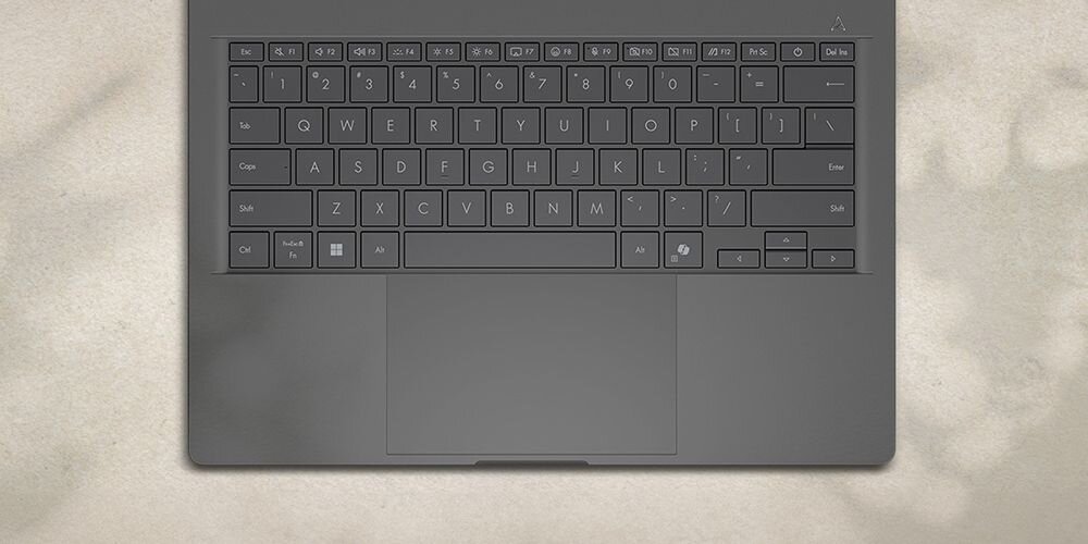 Widok z góry na klawiaturę laptopa ASUS Zenbook z klawiszami odpornymi na zabrudzenia i odciski palców w kolorze szarym na beżowym tle z naturalnymi teksturami - klawisze odporne na zabrudzenia