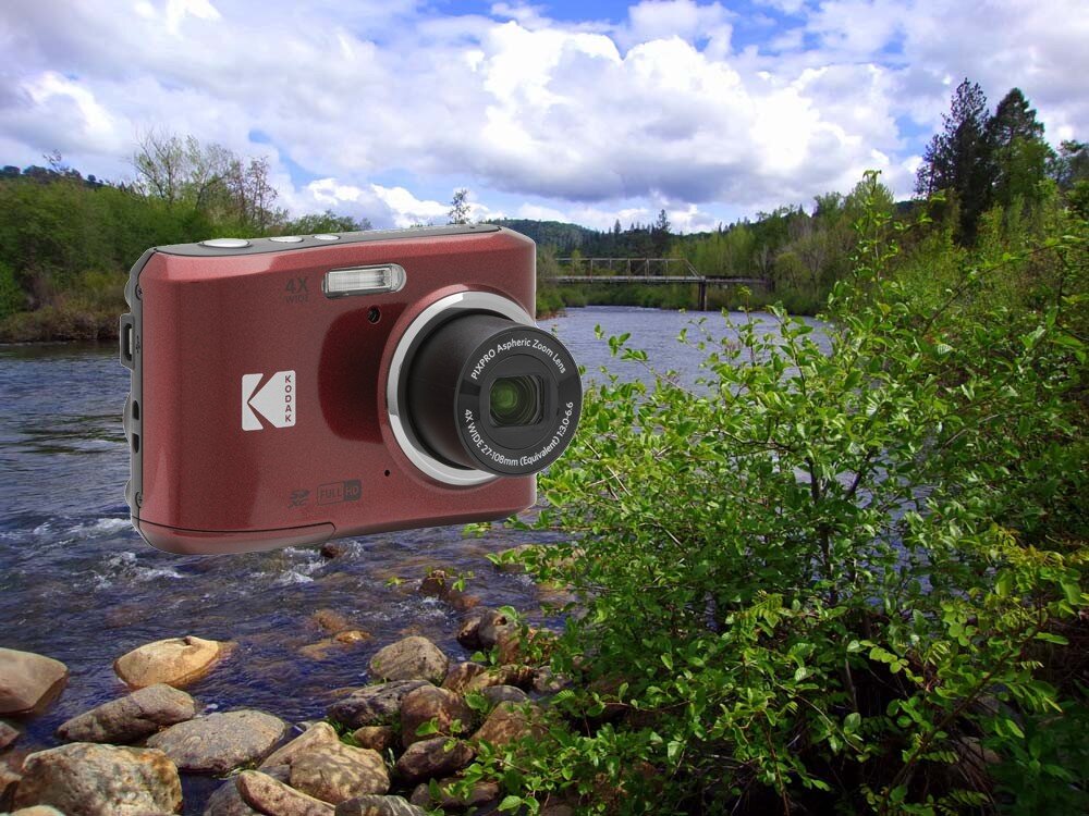 Na tle krajobrazu z rzeką i drzewami widoczny jest aparat fotograficzny z logo KODAK. Aparat ma obiektyw z napisem \'4x Optical Aspheric Zoom Lens\'.