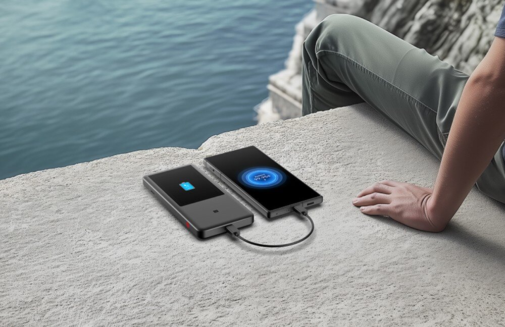 Router ZTE U60 Pro 5G Osoba siedząca na betonowym murku nad wodą, obok której router ZTE U60 Pro 5G ładuje smartfon poprzez kabel USB, pokazując funkcję powerbanku z szybkim ładowaniem.