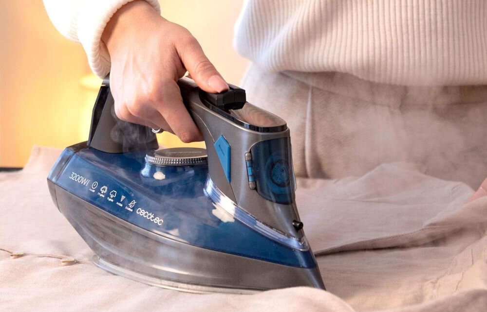 Żelazko CECOTEC IronHero 3200 Smart Absolute osoba trzyma żelazko ciemna obudowa przyciski pokrętło prasowanie materiału moc 3000 W podwójny element grzewczy blok nagrzewający przewód o długości 1,8 m swoboda ruchu wysoka wydajność szybkie łatwe wygodne prasowanie