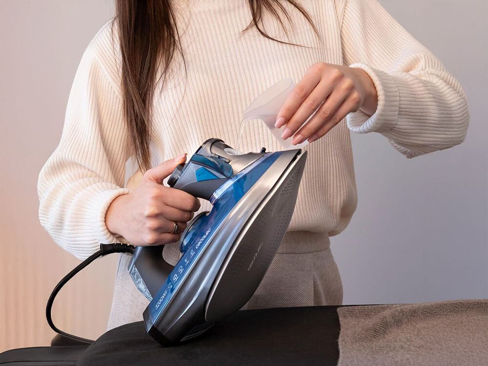 Żelazko CECOTEC IronHero 3200 Smart Absolute osoba trzyma żelazko wlewa płyn do obudowy urządzenia obudowa System antywapienny Cyclo Clean dłuższa żywotność żelazka zapobieganie osadzaniu się kamienia wewnętrzna filtracja wydajność na dłużej niezmienna moc