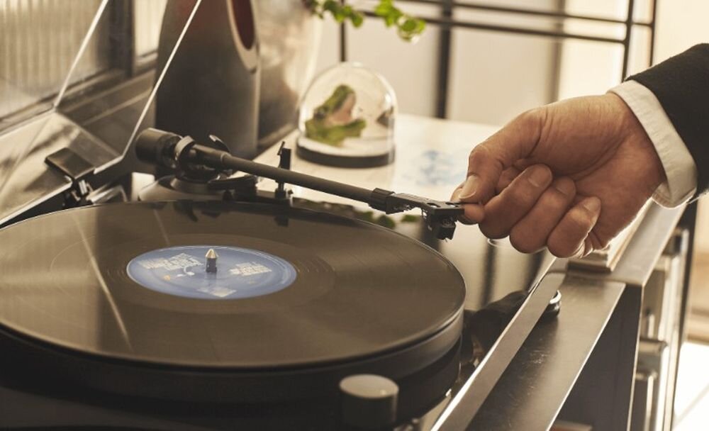 Gramofon AUDIO-TECHNICA AT-LPW50PB obudowa MDF 30 mm tłumienie drgań stabilna konstrukcja połysk, gramofon stojący na szafce, osoba trzymająca ramię gramofonu
