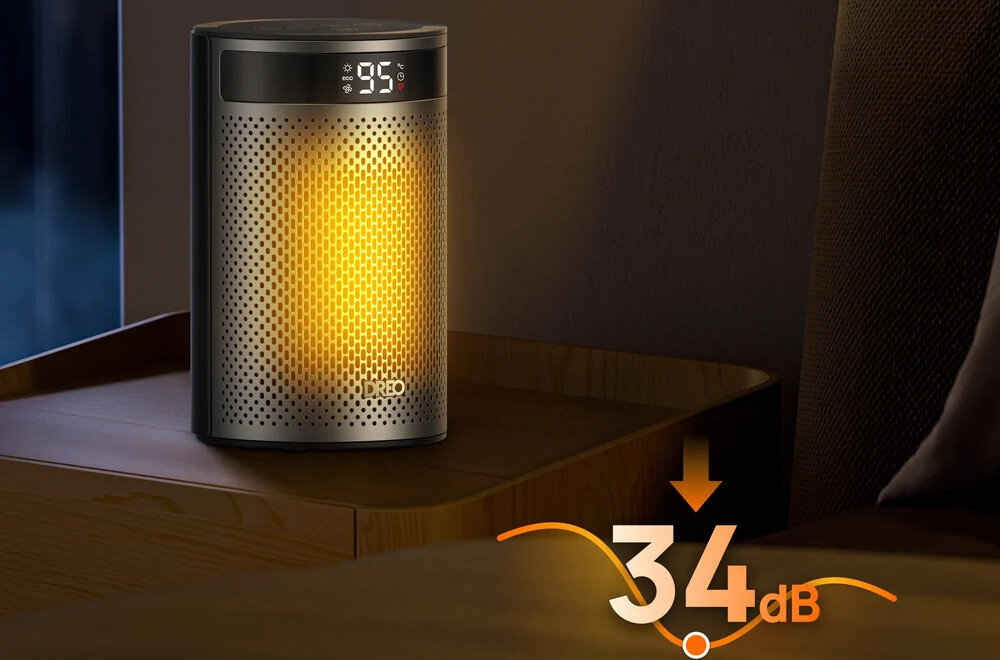 Na drewnianym stoliku stoi czarny grzejnik elektryczny z podświetleniem i wyświetlaczem pokazującym \'95\'. Na dole obrazu widnieje napis \'34 dB\' z pomarańczową strzałką skierowaną w dół.