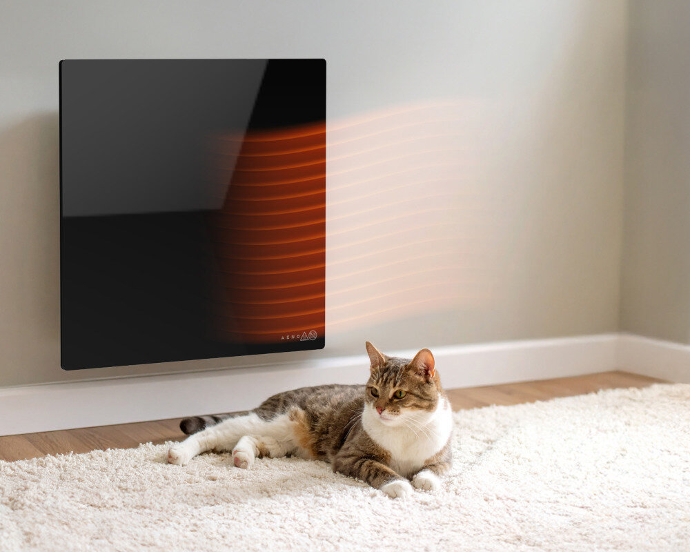 GRZEJNIK ELEKTRYCZNY AENO PREMIUM ECO SMART QUADRO 500W AGH0012S APP CZARNY Panel grzewczy na ścianie emitujący ciepło, a obok na dywanie leży kot bezpieczeństwo funkcja Child Lock blokada dzieci bezpieczna w dotyku powierzchnia komfort powiadomienie sygnał dźwiękowy alarm