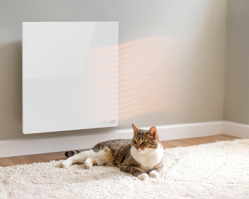 GRZEJNIK ELEKTRYCZNY AENO PREMIUM ECO SMART QUADRO 500W AGH0011S APP BIAŁY Panel grzewczy na ścianie emitujący ciepło, a obok na dywanie leży kot bezpieczeństwo funkcja Child Lock blokada dzieci bezpieczna w dotyku powierzchnia komfort powiadomienie sygnał dźwiękowy alarm