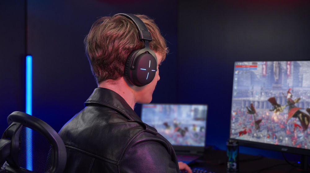 Słuchawki ACER Nitro II NHW200 Nauszne prezentacja słuchawek podczas korzystania chłopak siedzący przy komputerze i grający w grę w ciemnym pokoju
