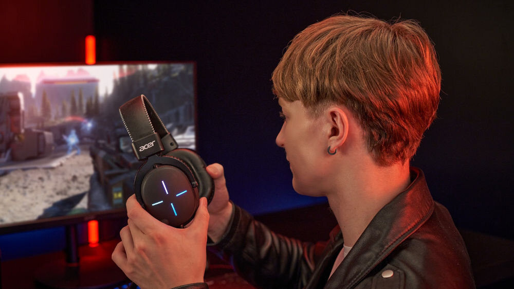 Słuchawki ACER Nitro II NHW200 Nauszne prezentacja słuchawek podczas zakładania chłopak siedzący przy komputerze i grający w grę w ciemnym pokoju przestrzenny dźwięk skuteczność