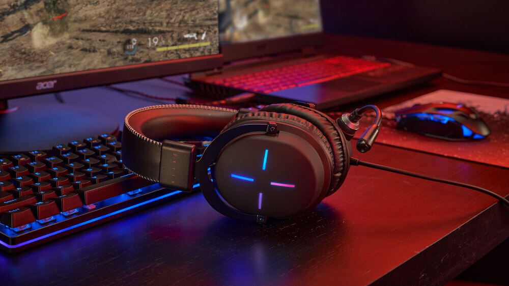 Słuchawki ACER Nitro II NHW200 Nauszne słuchawki leżące na biurku na klawiaturze w tle monitor laptop myszka ciemny pokój podświetlenie spójna estetyka gamingowy styl