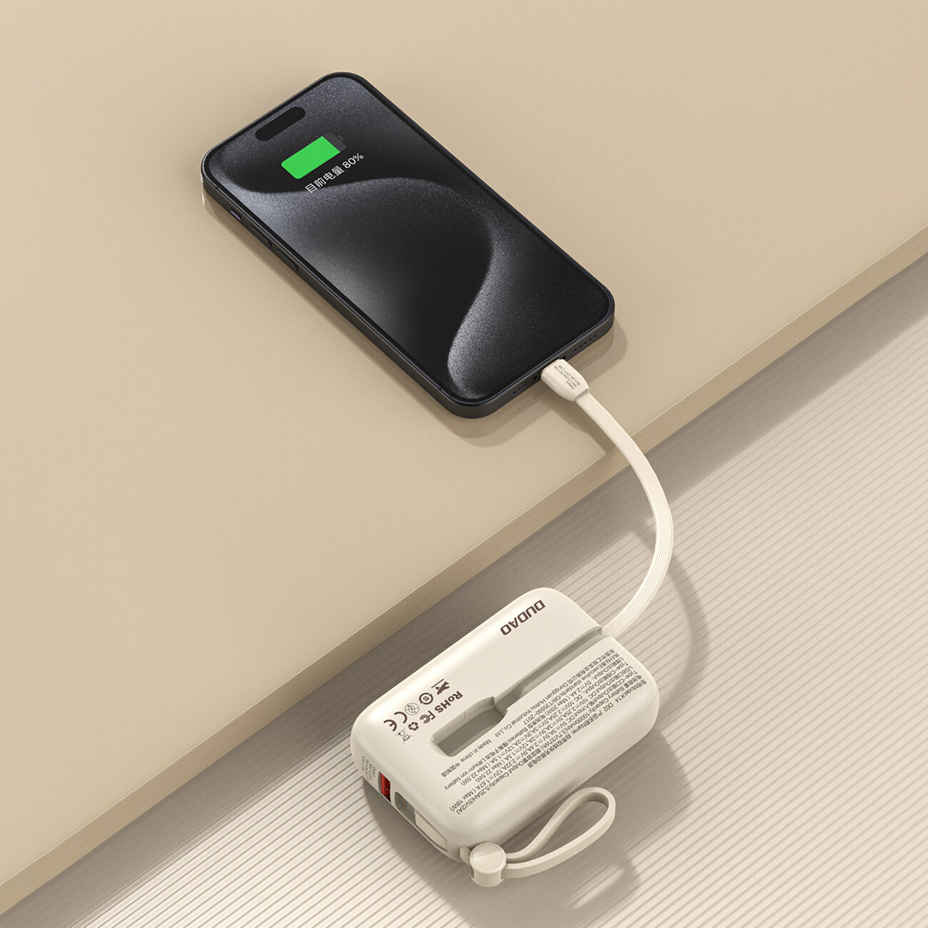 Na obrazie widać smartfon podłączony do beżowego powerbanku za pomocą kabla USB-C. Na ekranie telefonu widoczny jest wskaźnik ładowania z napisem \'80%\', a na powerbanku znajduje się logo \'DUDAO\'.
