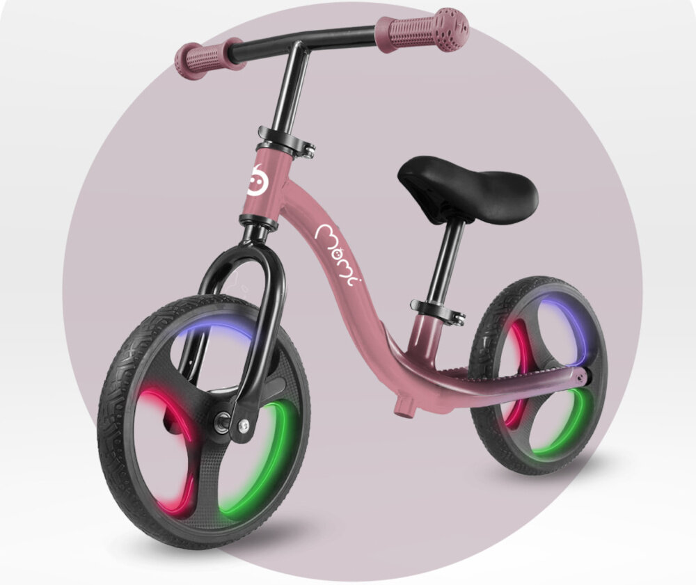 Rowerek biegowy MOMI Isoka Różowy jasne tło rowerek widoczny od przodu pod skosem włączone światła na kołach włączone światła na kołach koła ze wbudowanymi światłami LED aktywują się automatycznie podczas jazdy działają na zasadzie mechanizmu dynamo nie wymagają baterii ani ładowania efektowne podświetlenie kół przy każdym ruchu