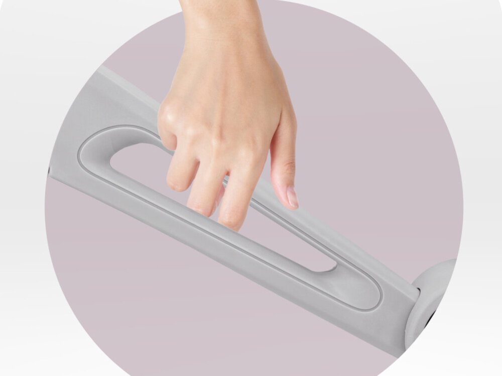 Rowerek biegowy MOMI Noru Szary zbliżenie na ramę osoba trzyma dłoń na otworze 10-calowa rama z wytrzymałego nylonu trwałość przy zachowaniu niskiej wagi 3 kg wygodny otwór łatwe przenoszenie rowerka ułatwia transport i przechowywanie