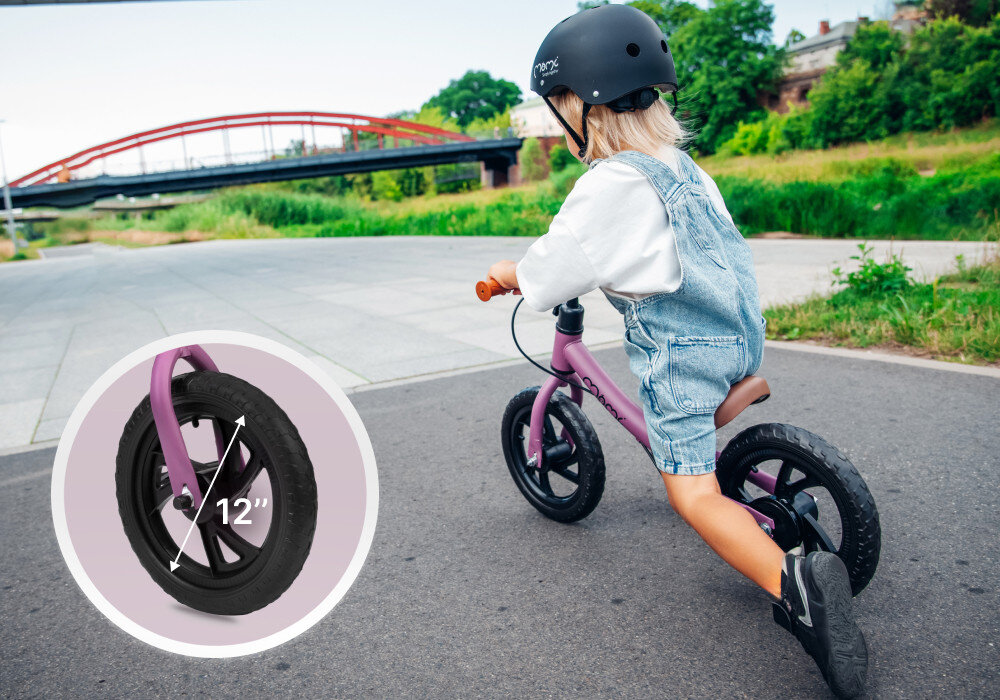 Rowerek biegowy MOMI Breki Fioletowy park droga rowerowa dziecko jedzie w kasku na rowerku po drodze w tle niebo drzewa krzewy niebo obok zdjęcie ze zbliżeniem na koło koła o średnicy 12 cali wykonane z pianki EVA odporne na przebicia brak konieczności pompowania eliminuje ryzyko awarii komfort rodzica nieprzerwana zabawa lekka struktura ułatwia jazdę płynne poruszanie