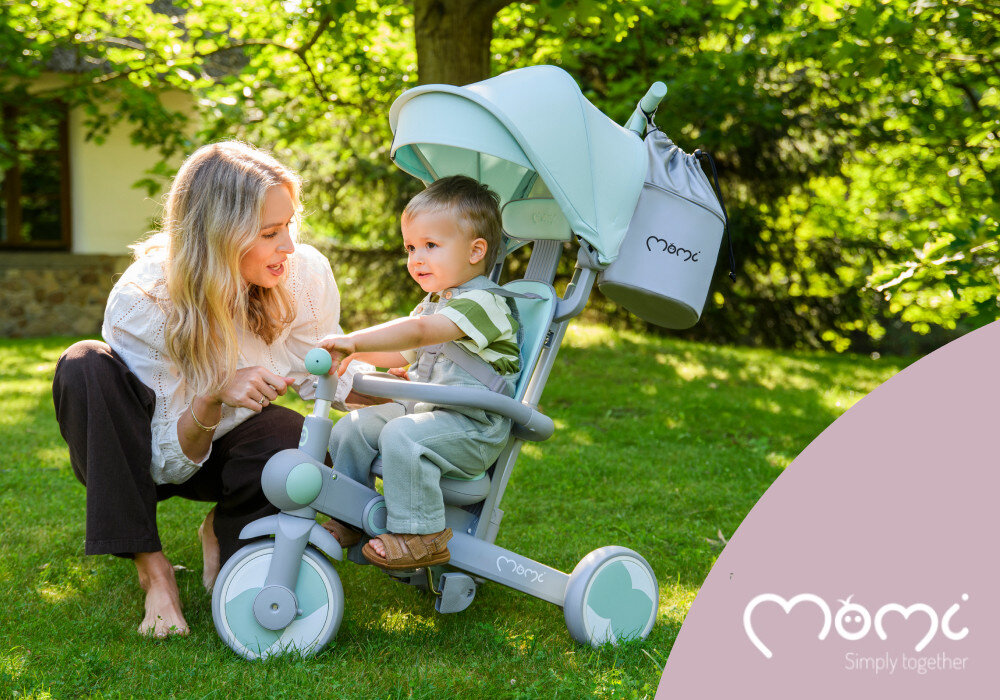 Rowerek trójkołowy MOMI Solivia 4w1 Opony Eva Zielony rączka trawnik dziecko siedzi na rowerku obok klęczy dorosła osoba w tle dom drzewa krzewy wielofunkcyjny rośnie z dzieckiem mobilność zabawa spacer