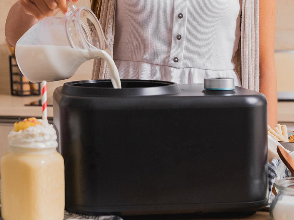 Maszynka do lodów CECOTEC Gelacy 800 Silnik osoba wlewa do czarnej maszynki do lodów śmietankę obok stoi przygotowany żółty koktajl  o mocy 100 W wysoka wydajność szybkie efektywne przygotowywanie lodów ciągła praca urządzenia długotrwałe użytkowanie optymalnie zmrożone dobrze wymieszane lody duża wydajność wymagające przepisy 