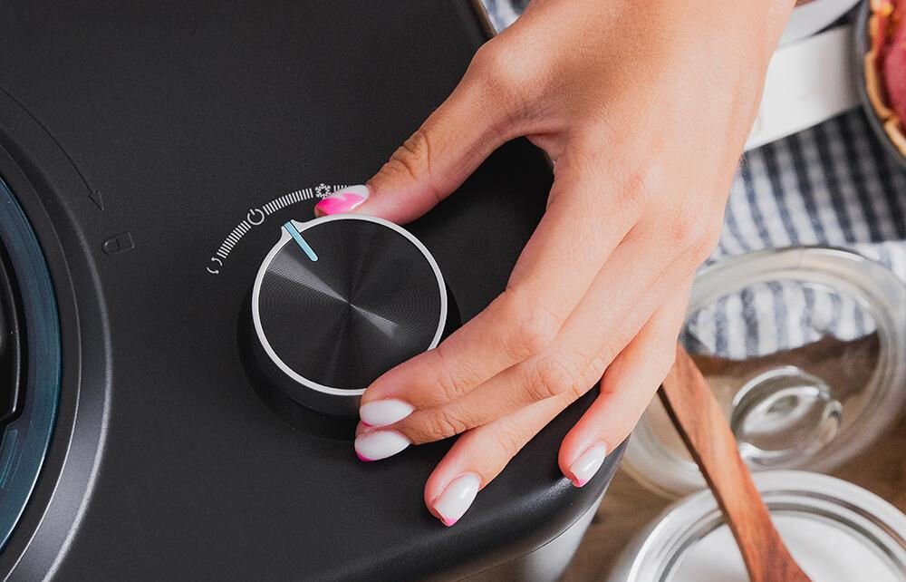 Maszynka do lodów CECOTEC Gelacy 800 osoba przekręca pokrętło na czarnej obudowie  wbudowane przyciski  funkcjonalne rozwiązanie ułatwienie obsługi pełna kontrola nad procesem ekran reaguje na delikatne dotknięcie intuicyjna szybka obsługa dostosowanie parametrów czas mrożenia prędkość mieszania składników optymalne rezultaty 