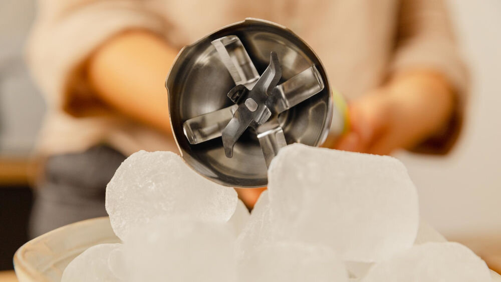 Blender CECOTEC Katana 15 TotalDestroy Smash B pojemnik kostki lodu osoba trzyma blender zbliżenie na czarne ostrze osiem trwałych ostrzy wykonanych w technologii BlackTitanium  pokryte czarnym tytanem bezproblemowe rozdrabnianie lodu orzechów twardych warzyw wyższa odporność na zużycie solidność wysoka jakość materiałów praktyczny wybór stylowy design wydajność trwałość 