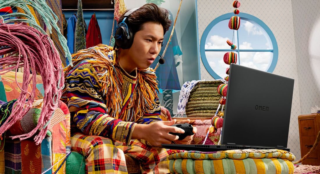 Mężczyzna siedzi na kanapie, grając w grę wideo na laptopie HP Omen 16. NVIDIA GeForce RTX  