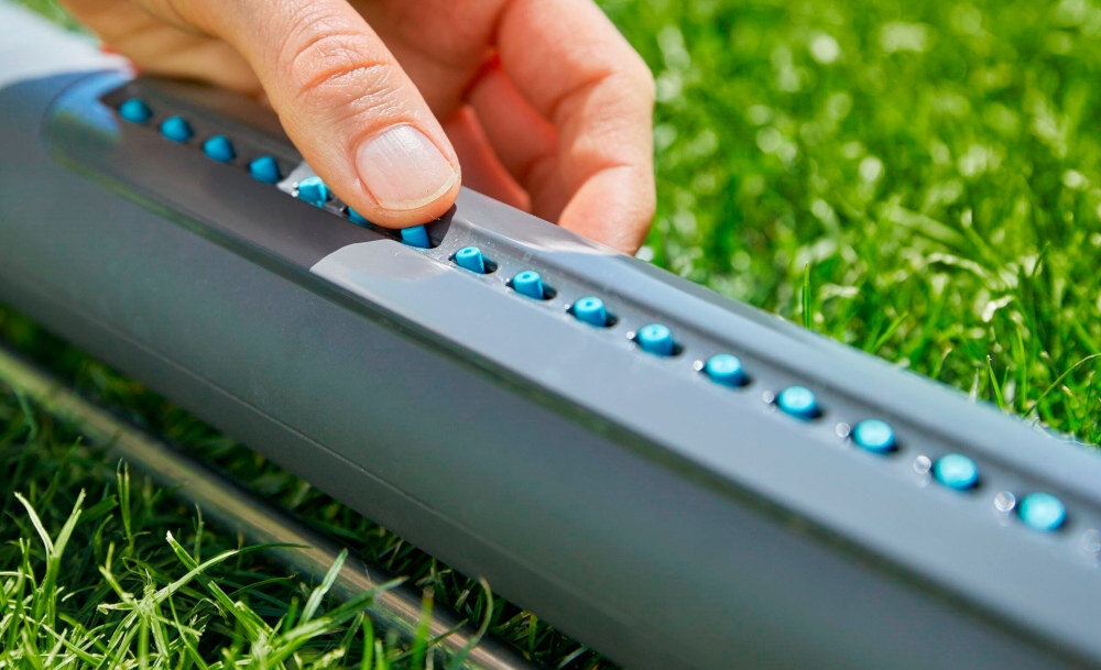 Zraszacz GARDENA Aquazoom S 18710-20 trawnik zraszacz na trawniku osoba przeciera palcami dysze dysze wykonano z miękkiego tworzywa sztucznego zabrudzenia wystarczy przetrzeć je palcami równomierne i niezakłócone zraszanie