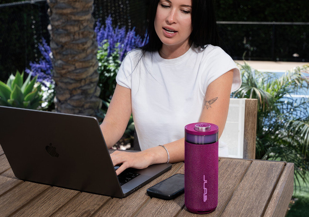 Głośnik JLAB Go Party LabSync do 100 głośników, synchronizacja dźwięku i świateł, osoba pracująca na laptopie, głośnik stojący na stole