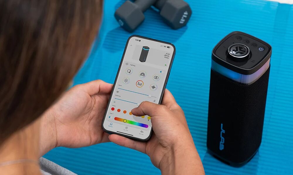 Głośnik mobilny JLAB Jbuds Party aplikacja sterowanie EQ4 ustawienia dźwięku, głośnik stojący na macie do ćwiczeń, osoba ustawiająca dźwięk w aplikacji na smartfonie