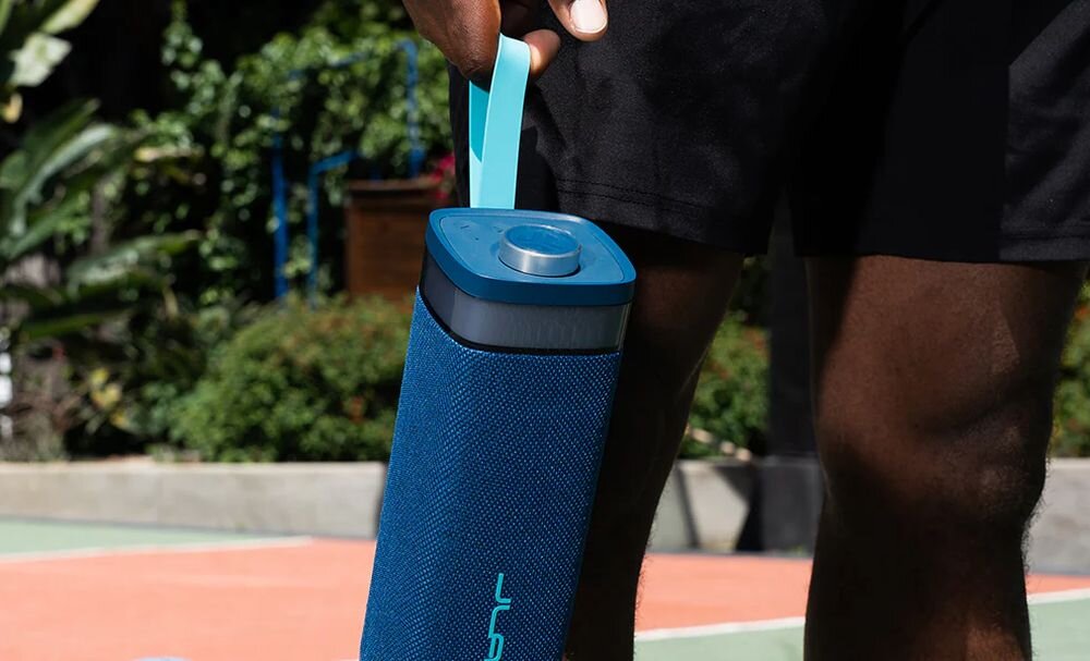 Głośnik mobilny JLAB Jbuds Party czas pracy 12 godzin akumulator 5000 mAh USB-C, osoba trzymająca głośnik za pasek