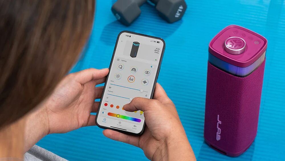 Głośnik mobilny JLAB Jbuds Party aplikacja sterowanie EQ4 ustawienia dźwięku, głośnik stojący na macie do ćwiczeń, osoba ustawiająca dźwięk w aplikacji na smartfonie