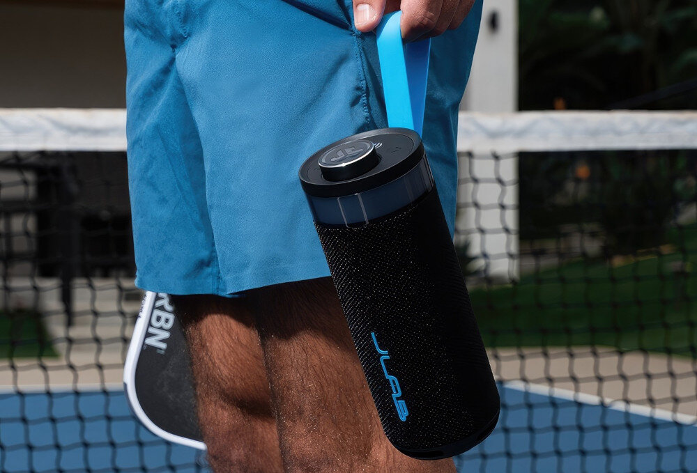 Głośnik JLAB Go Party stereo pairing, lewy i prawy kanał, przestrzenny dźwięk, osoba trzymająca głośnik za pasek