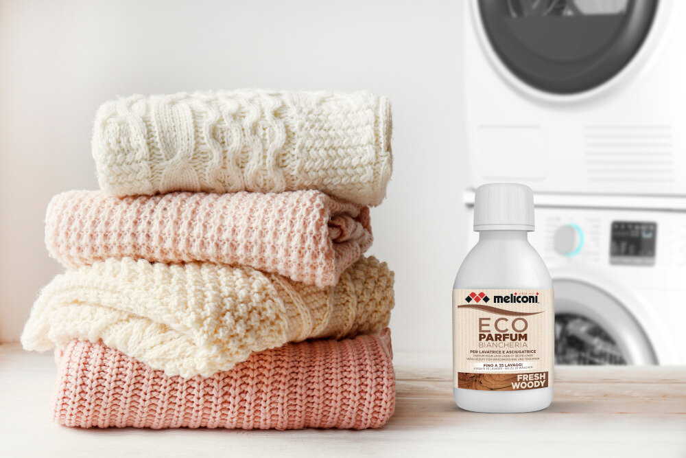 KROPLE ZAPACHOWE MELICONI Obok starannie złożonego stosu ubrań znajduje się butelka Meliconi ECO PARFUM w wariancie Fresh Woody. Scena podkreśla efekt działania produktu — świeżą i zadbaną odzież po praniu nuty mydlane Długotrwały intensywny zapach świeżość ubrań nuty mydlane zapach drzewno-orientalny świeżość na długo