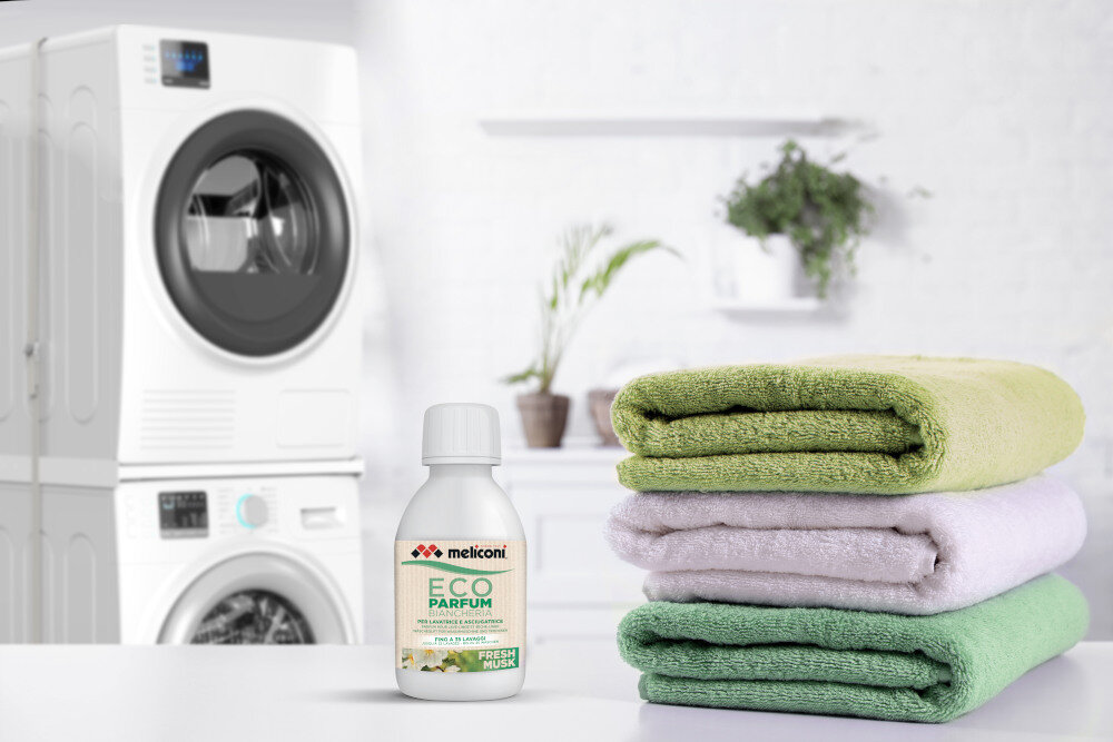 KROPLE ZAPACHOWE MELICONI Obok starannie złożonego stosu ubrań znajduje się butelka Meliconi ECO PARFUM w wariancie Fresh Musk. Scena podkreśla efekt działania produktu — świeżą i zadbaną odzież po praniu nuty mydlane Długotrwały intensywny zapach świeżość ubrań nuty mydlane zapach piżma bawełny świeżość na długo