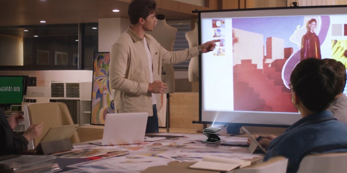 Projektor AURZEN Zip Tri-Fold Mini HD LED LCoS 500 ANSI autofocus, osoba trzymająca smartfon w ręku, projektor wyświetlający obraz na ekranie projekcyjnym na spotkaniu biznesowym