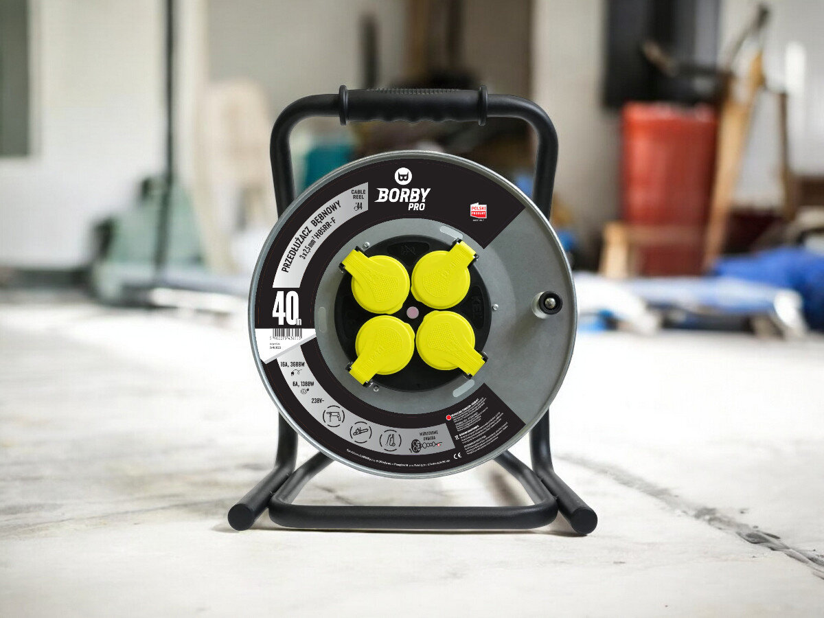 Przedłużacz bębnowy BORBY BY-02-36553 (40 m), solidne, odległość, zasięg, dystans, przedłużacz frontem na wprost z 4 wejściami stoi, w tle trwają prace remontowo-budowlane