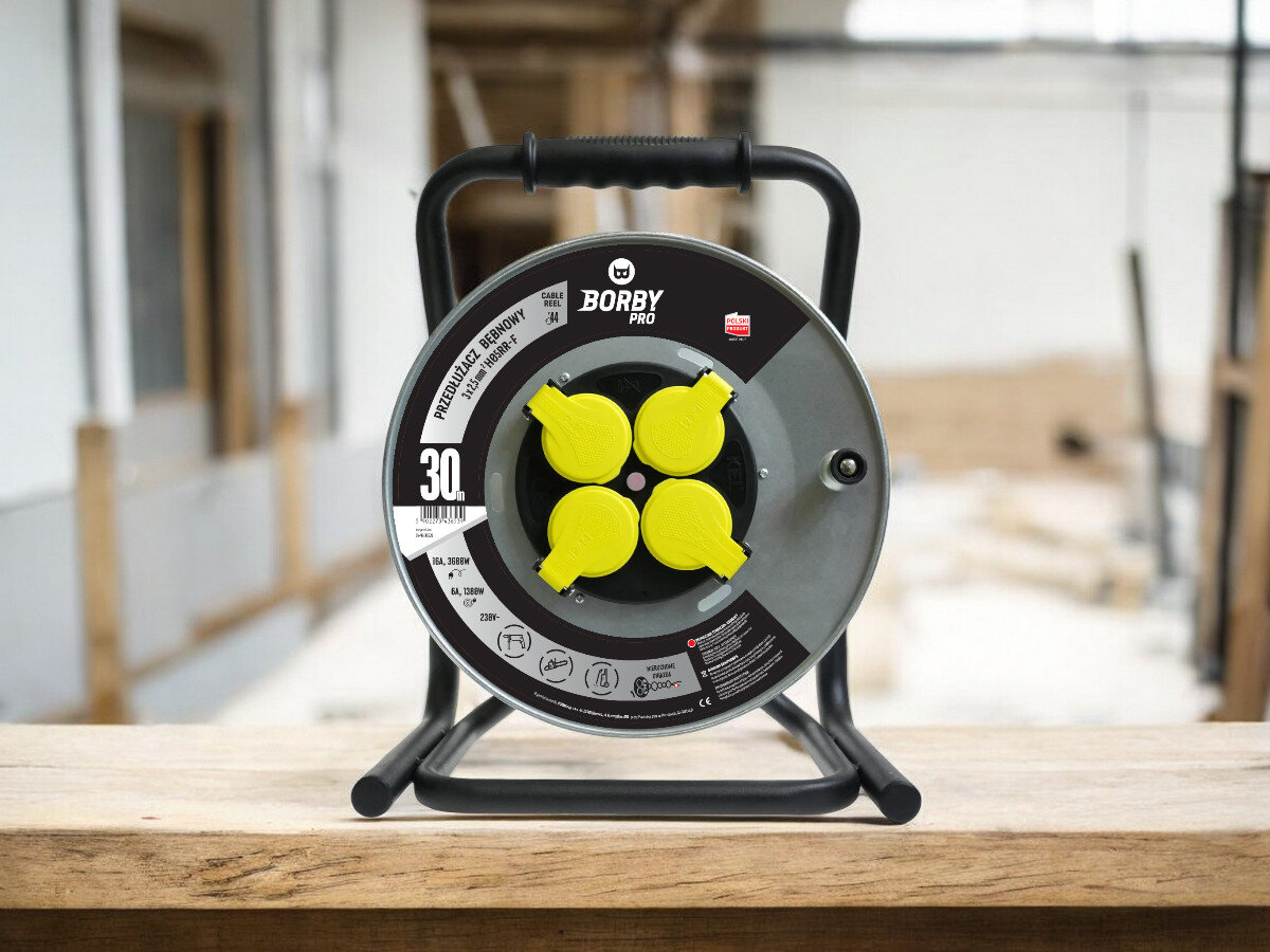 Przedłużacz bębnowy BORBY BY-02-36539 (30 m), solidne, odległość, zasięg, dystans, przedłużacz frontem na wprost z 4 wejściami stoi, w tle trwają prace remontowo-budowlane