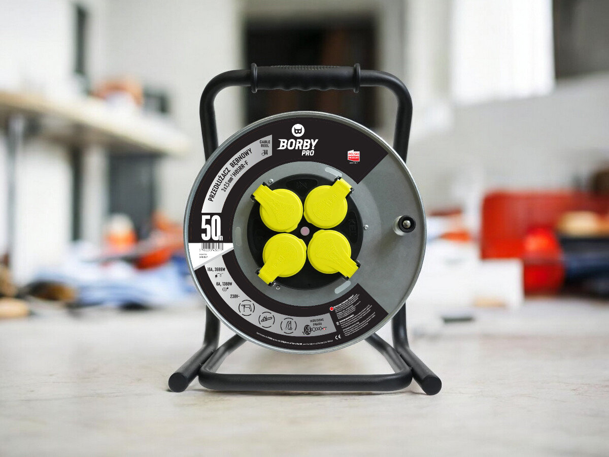 Przedłużacz bębnowy BORBY BY-02-36577 (50 m), solidne, odległość, zasięg, dystans, przedłużacz frontem na wprost z 4 wejściami stoi, w tle trwają prace remontowo-budowlane