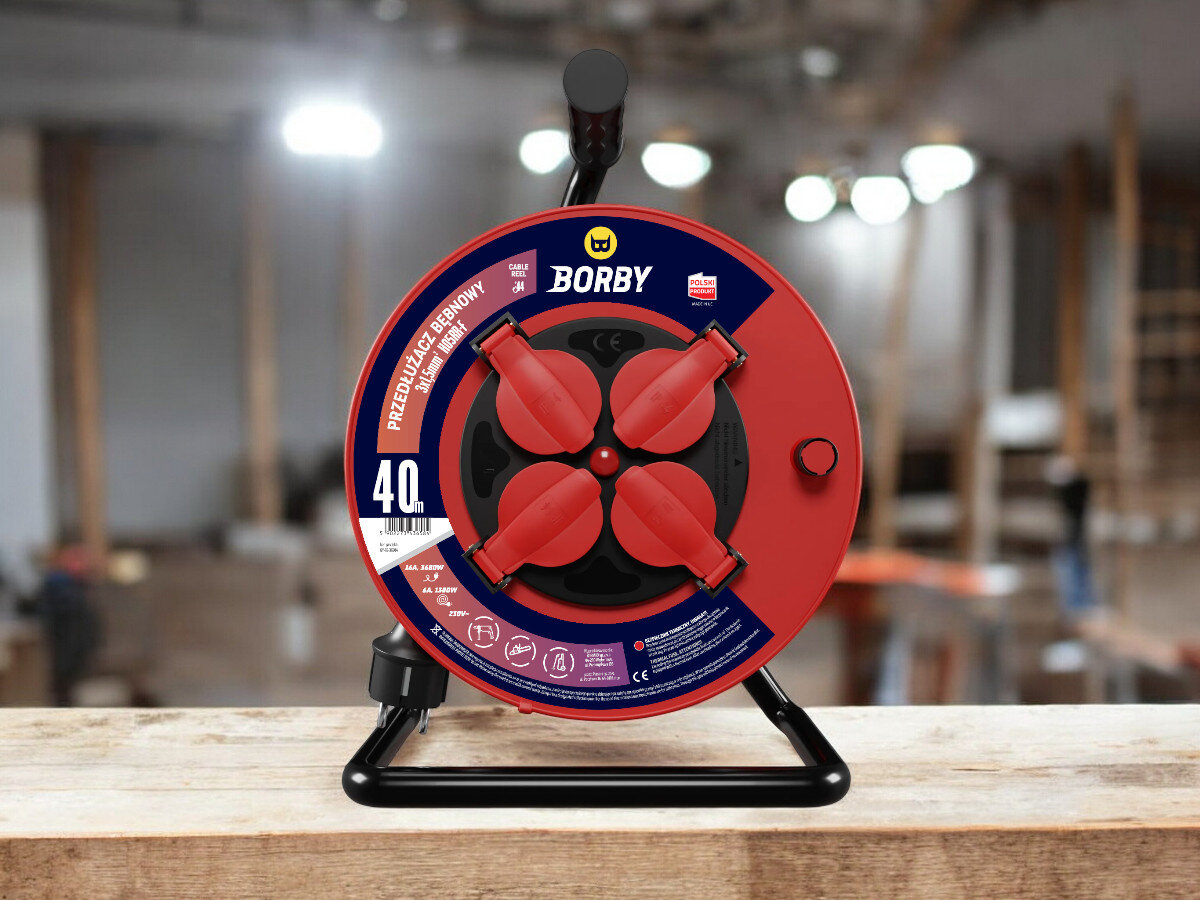 Przedłużacz bębnowy BORBY BY-02-36621 (40 m), solidne, odległość, zasięg, dystans, przedłużacz frontem na wprost z 4 wejściami stoi, w tle trwają prace remontowo-budowlane