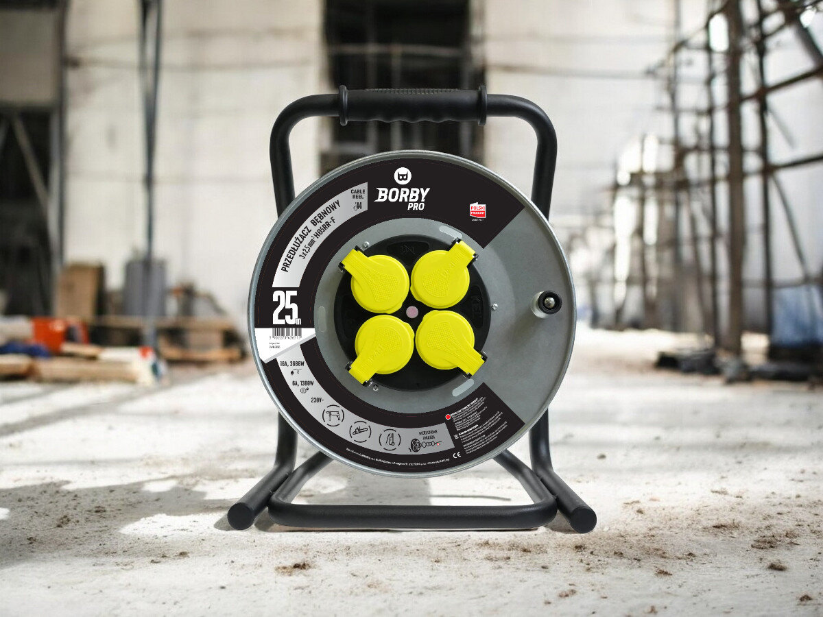 Przedłużacz bębnowy BORBY BY-02-36515 (25 m), solidne, odległość, zasięg, dystans, przedłużacz frontem na wprost z 4 wejściami stoi, w tle trwają prace remontowo-budowlane