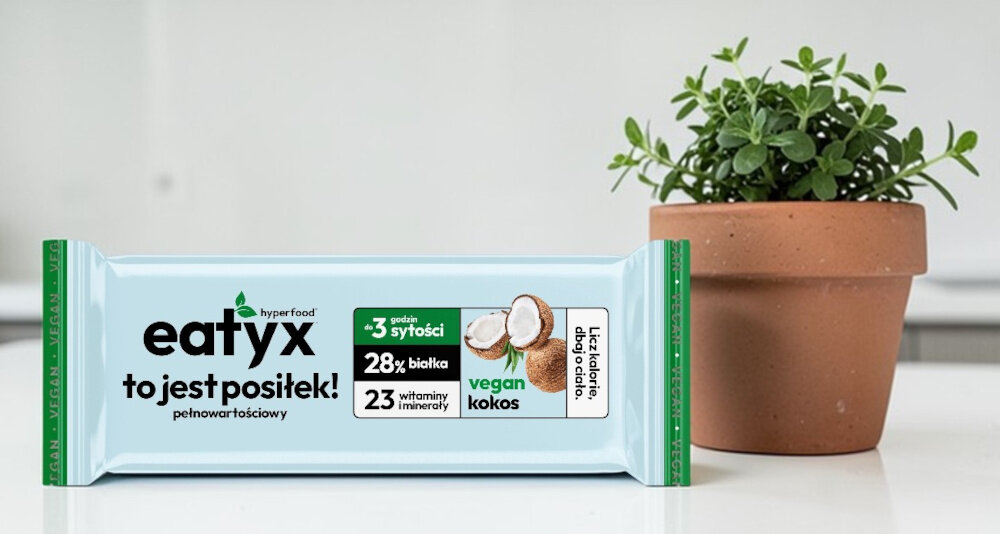 Baton proteinowy EATYX Hyperfood Kokosowy (8 x 60 g) kuchnia blat baton leży na blacie obok stoi kwiatek w doniczce produkt odpowiedni dla osób żyjących w szybkim tempie dbających o skład diety stosujących dietę wegańską, bezglutenową lub bezlaktozową wygodnego źródła energii