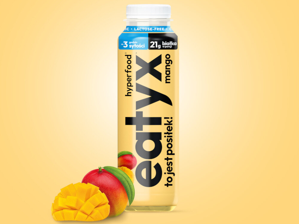 Posiłek w płynie EATYX Hyperfood Mango (300 ml) butelka posiłku na żółtym m tle obok owoce mango 21 witamin i minerałów biotyna (8.4 µg) witamina B12 (0,6 µg) chrom (6,6 µg) selen (9,3 µg) cynk (3,3 mg) wapń (570 mg) wspierają zdrowie skóry, włosów, paznokci i metabolizmu energetycznego