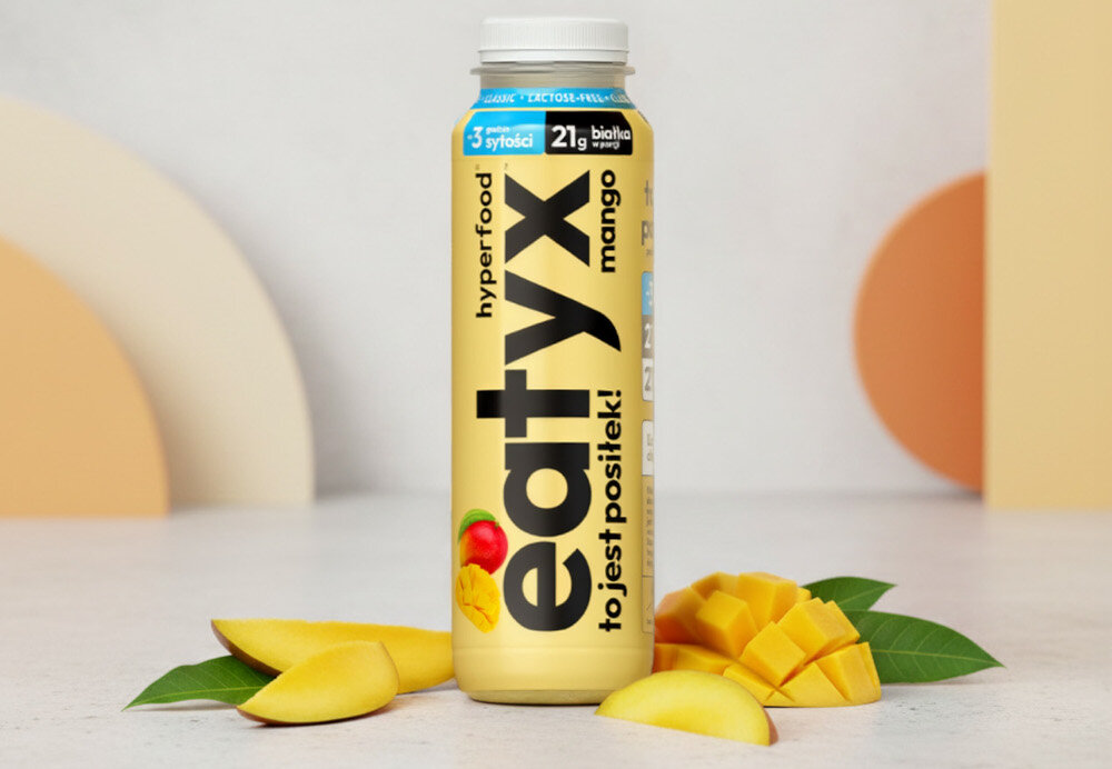 Posiłek w płynie EATYX Hyperfood Mango (300 ml) butelka posiłku na białym tle obok owoce mango w tle pomarańczowe elementy ściany bazuje na białkach mleka bez laktozy łagodny dla układu pokarmowego dla osób z nietolerancją laktozy nie zawiera glutenu ani konserwantów nie zawiera dodatku cukru lekkostrawny, pełnowartościowy posiłek w płynie