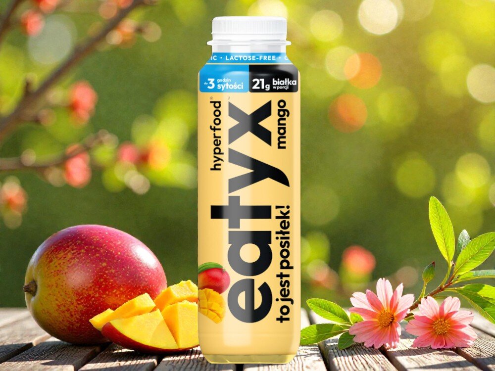 Posiłek w płynie EATYX Hyperfood Mango (300 ml) drewniana podłoga butelka stoi na podłodze obok butelki owoce mango rozmazane zielone tło olej słonecznikowy źródło kwasów omega-6 i witaminy E chroni komórki przed stresem oksydacyjnym oraz wspiera serce, skórę i odporność węglan wodorotlenku magnezu magnez niezbędny dla kości, mięśni i układu nerwowego