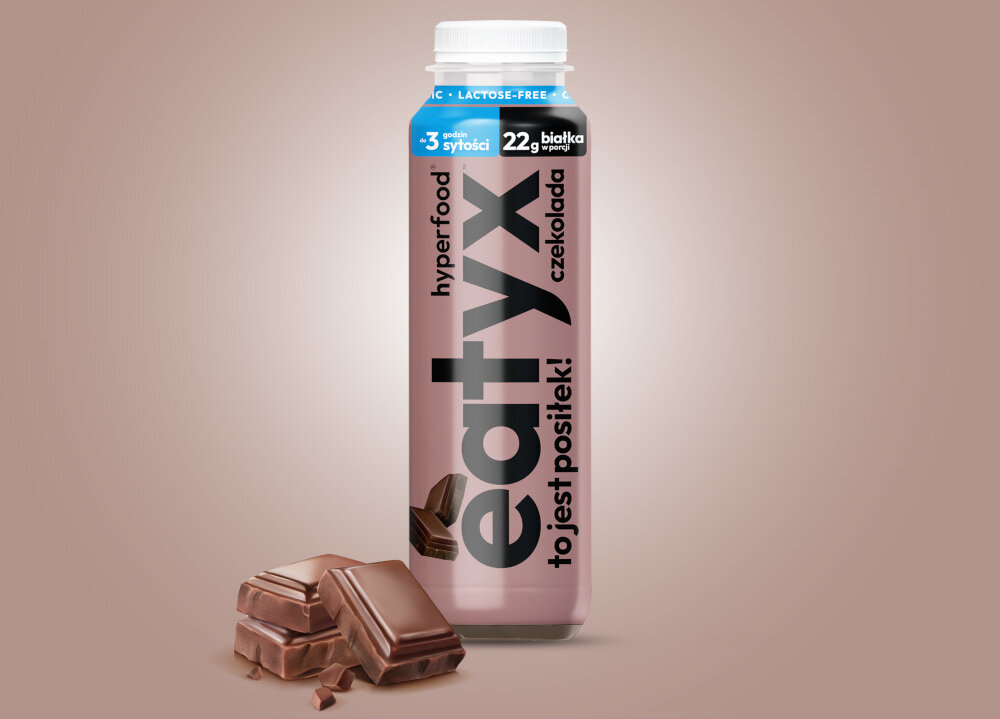 Posiłek w płynie EATYX Hyperfood Czekoladowy (300 ml) butelka posiłku na brązowym m tle obok kostki czekolady 21 witamin i minerałów biotyna (8.4 µg) witamina B12 (0,6 µg) chrom (6,6 µg) selen (9,3 µg) cynk (3,6 mg) wapń (570 mg) wspierają zdrowie skóry, włosów, paznokci i metabolizmu energetycznego