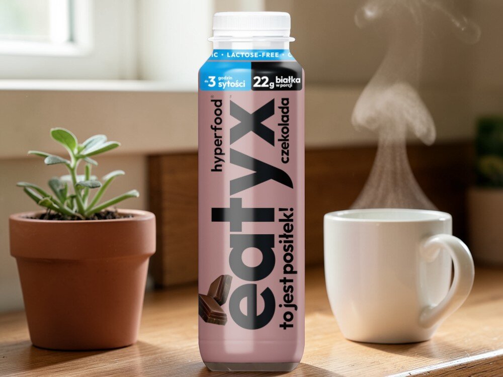 Posiłek w płynie EATYX Hyperfood Czekoladowy (300 ml) pokój stół butelka posiłku stoi na blacie obok kubek kwiatek w doniczce bazuje na białkach mleka bez laktozy łagodny dla układu pokarmowego dla osób z nietolerancją laktozy nie zawiera glutenu ani konserwantów nie zawiera dodatku cukru lekkostrawny, pełnowartościowy posiłek w płynie