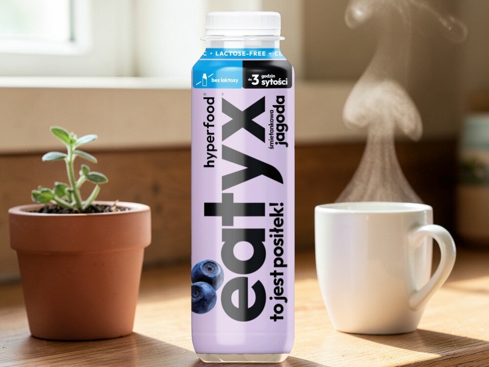 Posiłek w płynie EATYX Hyperfood Śmietankowo-jagodowy (300 ml) pokój stół butelka posiłku stoi na blacie obok kubek kwiatek w doniczce bazuje na białkach mleka bez laktozy łagodny dla układu pokarmowego dla osób z nietolerancją laktozy nie zawiera glutenu ani konserwantów nie zawiera dodatku cukru lekkostrawny, pełnowartościowy posiłek w płynie