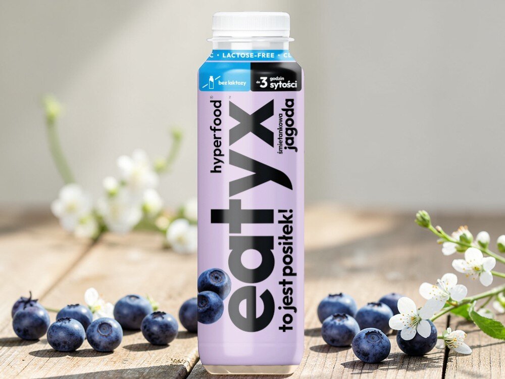 Posiłek w płynie EATYX Hyperfood Śmietankowo-jagodowy (300 ml) jasne tło butelka ustawiona na drewnianym blacie wokół butelki owoce jagód i białe kwiatki olej słonecznikowy źródło kwasów omega-6 i witaminy E chroni komórki przed stresem oksydacyjnym oraz wspiera serce, skórę i odporność węglan wodorotlenku magnezu magnez niezbędny dla kości, mięśni i układu nerwowego