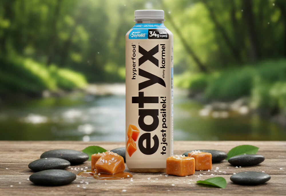 Posiłek w płynie EATYX Hyperfood Słony Karmel (500 ml) drewniana podłoga butelka stoi na podłodze obok butelki kostki karmelu w tle strumyk rozmazane zielone tło olej słonecznikowy źródło kwasów omega-6 i witaminy E chroni komórki przed stresem oksydacyjnym oraz wspiera serce, skórę i odporność węglan wodorotlenku magnezu magnez niezbędny dla kości, mięśni i układu nerwowego