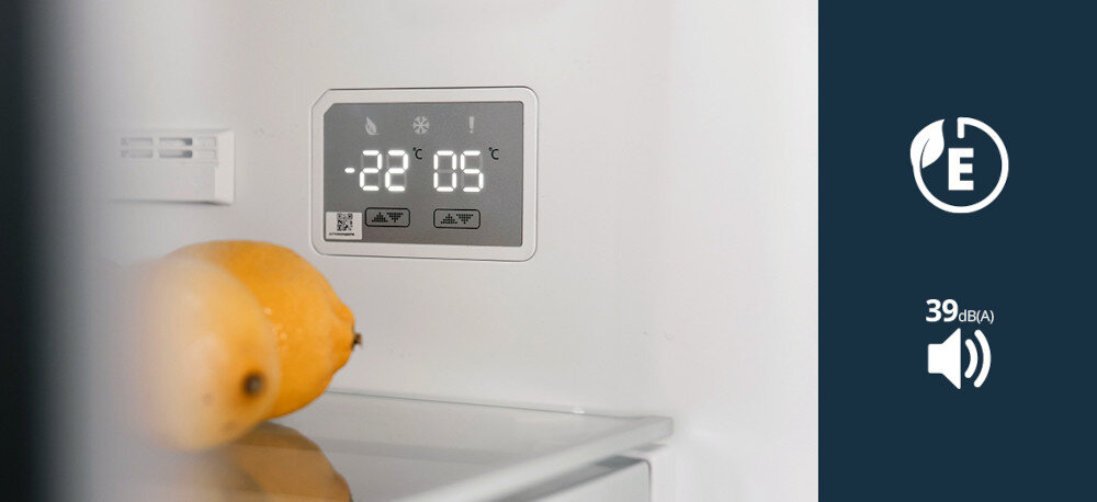Lodówka VESTFROST VR-FB373-2E2RD Zdjęcie pokazuje wnętrze lodówki z elektronicznym panelem sterowania, na którym wyświetlane są jasne cyfry temperatury chłodziarki i zamrażarki, a na półce poniżej leżą żółte owoce. Po prawej stronie na granatowym tle znajdują się piktogram klasy energetycznej E oraz ikona głośnika z wartością 39 dB(A), podkreślające energooszczędność i cichą pracę urządzenia klasa energetyczna E niskie zużycie energii 250 kWh rocznie cicha praca 41 dB energooszczędność ekologia