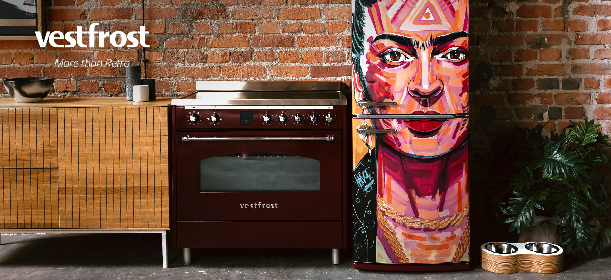 Kuchnia VESTFROST VC-993WNPIBR.2 Zdjęcie przedstawia bordową kuchenkę gazową na tle ceglanej ściany, ustawioną obok stylowej lodówki retro. Całość utrzymana jest w industrialnym, loftowym stylu z drewnianą komodą po lewej stronie. Połączenie czerni i naturalnego drewna nadaje wnętrzu elegancji oraz klasycznego charakteru.