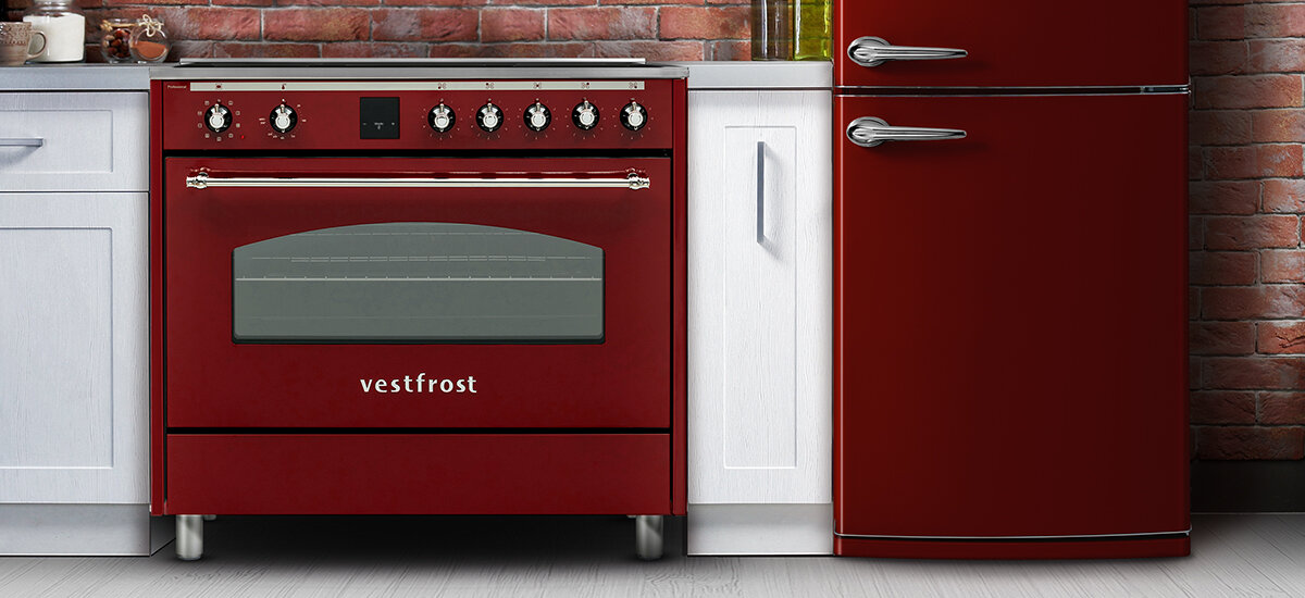 Kuchnia VESTFROST VC-993WNPIBR.2 Na zdjęciu widać kuchenkę, lodówkę i drewnianą komodę, ukazane w szerszym ujęciu z logotypem marki i hasłem w górnym rogu. Wnętrze charakteryzuje się ceglaną ścianą, wyeksponowanymi rurami i loftowym klimatem. Kompozycja podkreśla unikalny styl retro połączony z funkcjonalnością sprzętów design bordowo satynowe wykończenie styl retro elegancki wygląd technologie klasyczny styl praktyczność estetyka Vestfrost retro